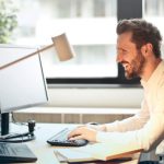 Email - Man in White Dress Shirt Sitting on Black Rolling Chair While Facing Black Computer Set and Smiling