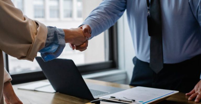 Spam Folder - Crop unrecognizable coworkers in formal wear standing at table with laptop and documents while greeting each other before meeting