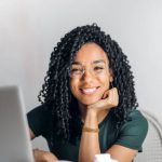 Content - Happy ethnic woman sitting at table with laptop