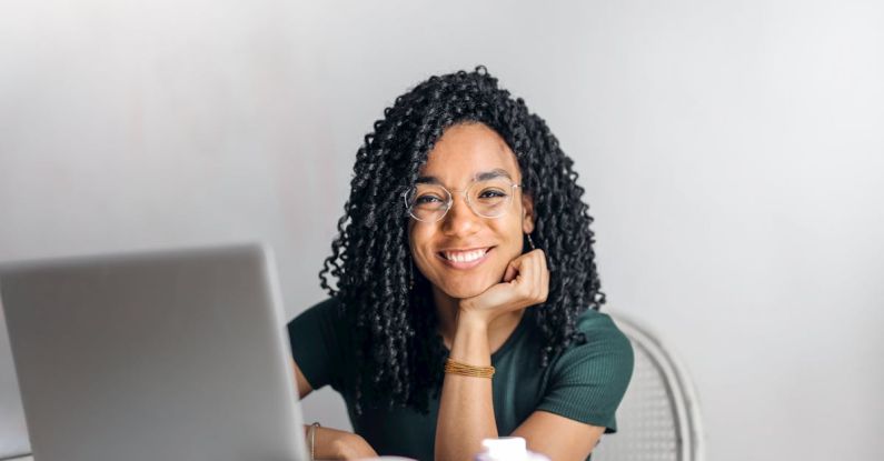 Content - Happy ethnic woman sitting at table with laptop