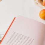 Product Pages - From above of opened book placed on white table near cotton sack with natural ripe apricots